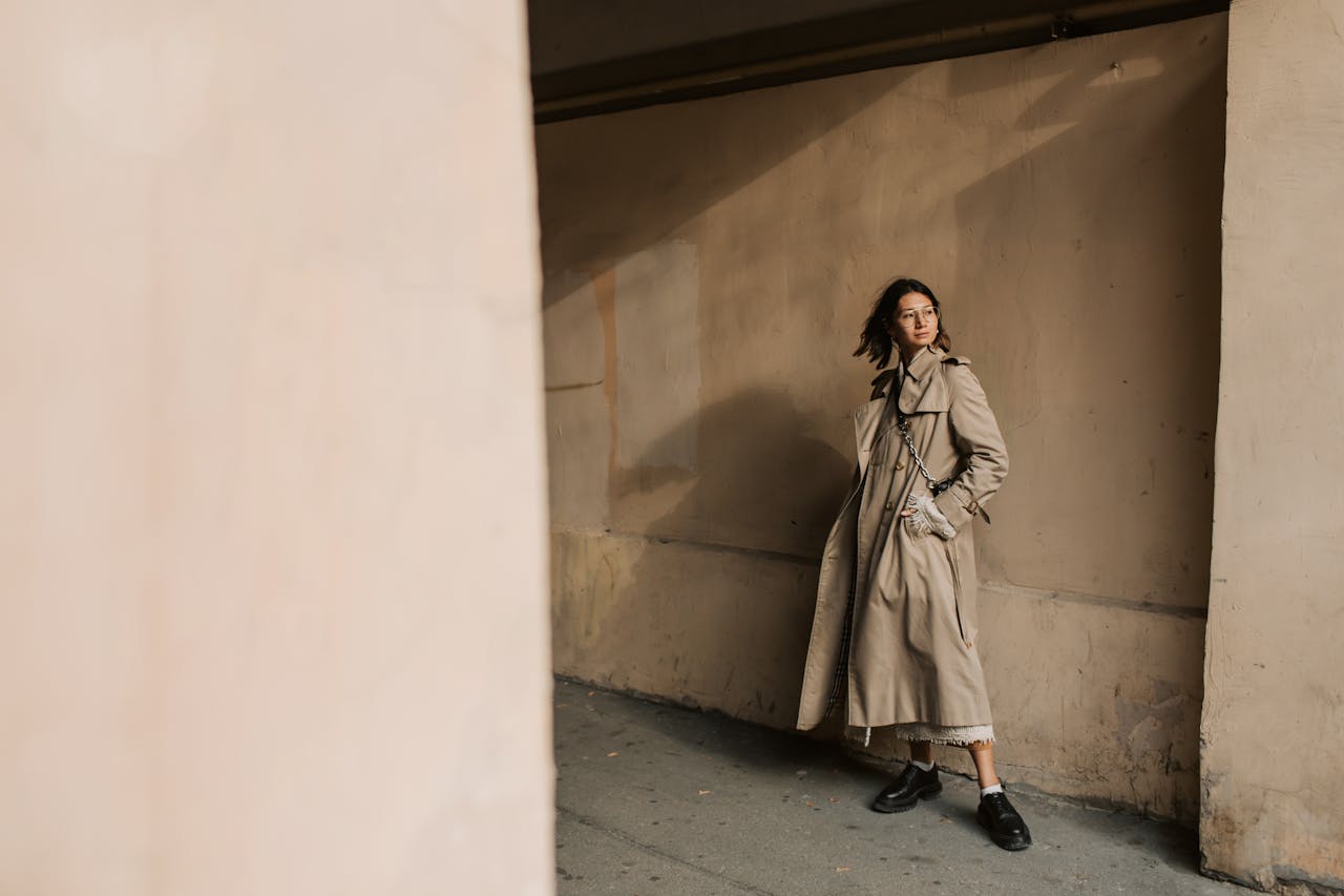 Stylish woman posing in a trench coat against a concrete wall with urban background.